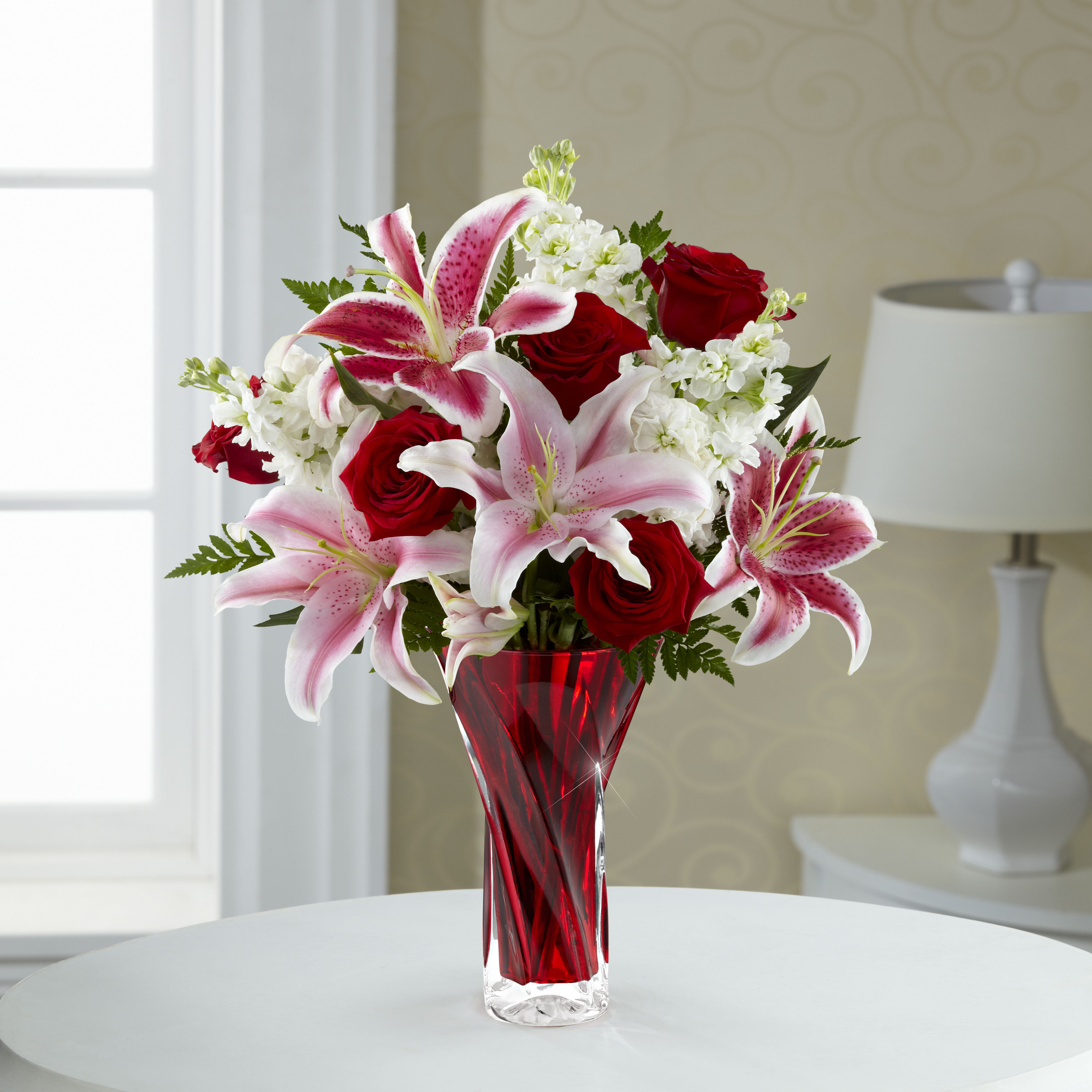 Elegant bouquet of pink lilies and red roses in a clear glass vase.